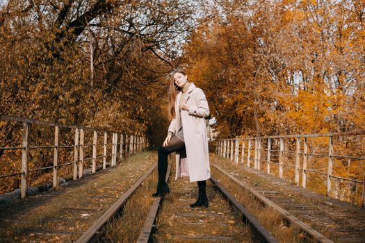 A beautiful long-haired woman walks through the autumn streets. Railway, autumn leaves, a woman in a light coat.