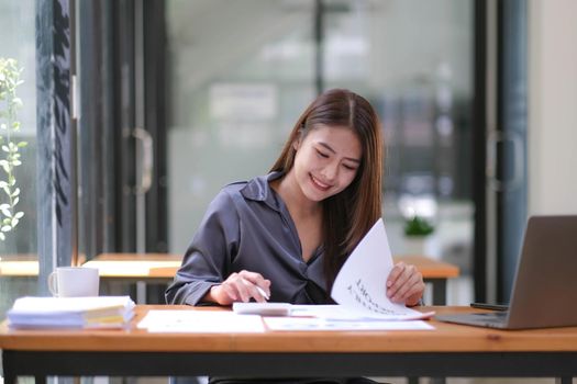 Asian Businesswoman using a calculator and laptop computer for doing math finance on a wooden desk, tax, accounting, statistics report and analytical research concept..