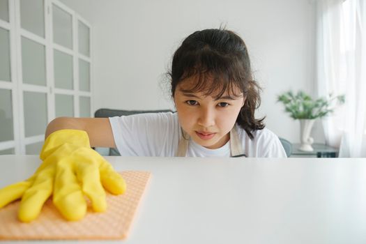 Woman cleaning, wiping and disinfecting tabletop with wipe sponge and wearing protective gloves in living room at home. Woman doing chores at home with effort. Housekeeping concept.