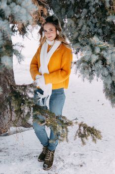 Teen blonde in a yellow sweater outside in winter. A teenage girl on a walk in winter clothes in a snowy forest.