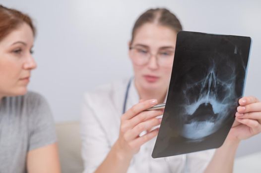 A woman doctor and a patient at the reception are discussing an x-ray of the sinuses
