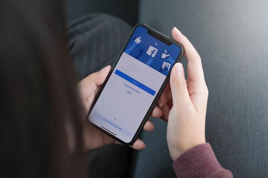 CHIANG MAI ,THAILAND AUG 10 2022 : Woman holding a iPhone X with social Internet service Facebook on the screen..