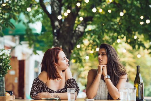 Two young beautiful women girlfriends talking in an outdoor cafe, gossiping, telling news together. Female friendship