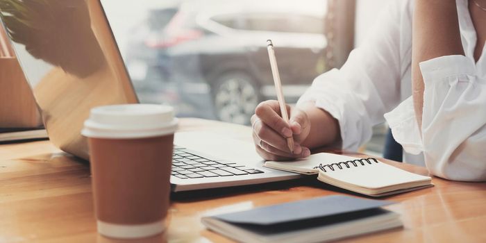 Close up image of a woman writing and taking note on notebook with laptop in office..