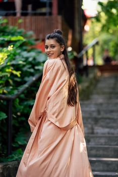 Young smiling woman on walking in the park wearing robe, summer day