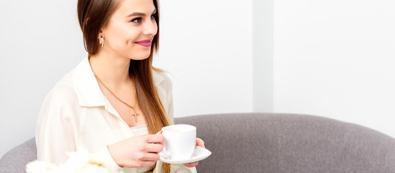 Female caucasian client with a cup of coffee in his hands smiling at a doctor's appointment