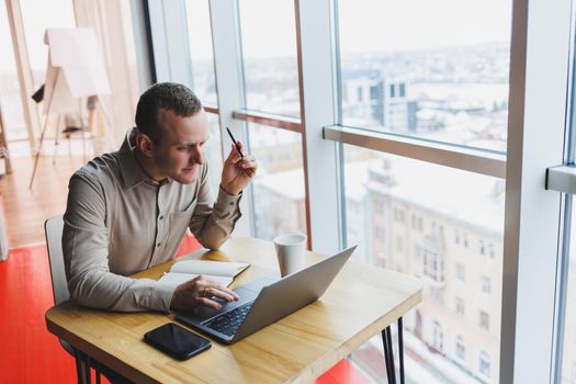 Smart young man looking for information on a website and working as a freelancer on developing a graphic project on a modern laptop using a wireless internet connection in a cafe interior