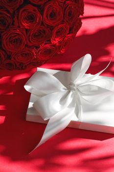 Happy holidays, luxe shopping and love gifts concept - Luxury holiday silk gift box and bouquet of roses on red background, romantic surprise and flowers as birthday or Valentines Day present