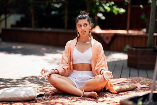 Young woman is practising yoga sitting on a wooden podium in the garden in the sunny morning