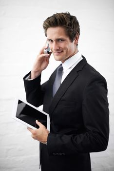 Communication is an important part of business. A handsome young businessman talking on his phone while holding his tablet