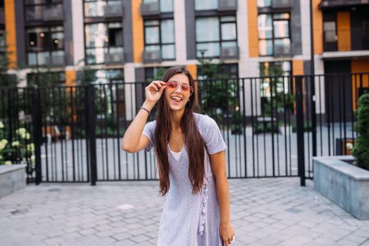 Summer time. Happy cheerful girl laughs on the background of large building in city.