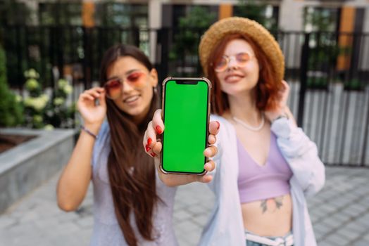 Two lovely girlfriends shows their phone to the camera