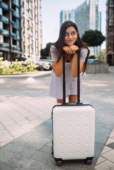 Stylish woman with suitcase looking at camera at the street
