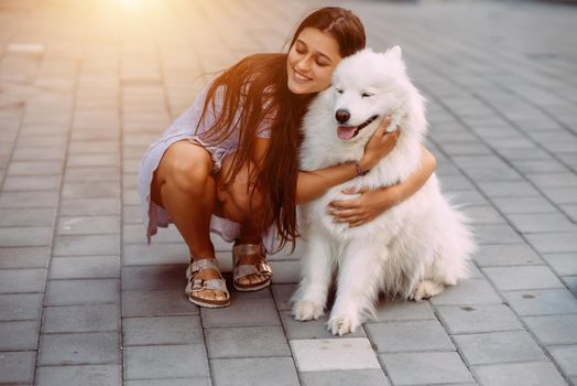 A young woman hugs a big dog at sunset in summer