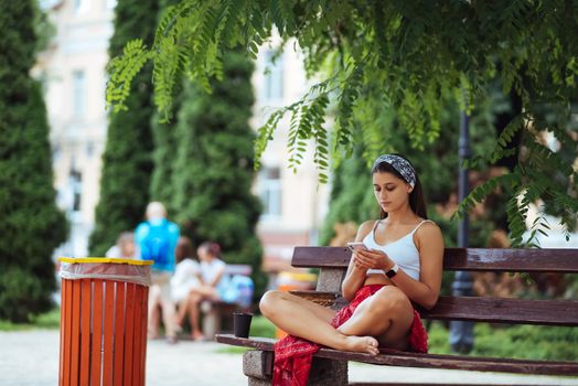Happy girl using a smartphone in a city park sitting on a bench