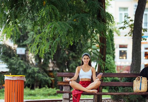 A young girl sits in a lotus position on a bench.