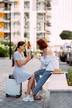 Two young women on a city street with a globe in their hands. Travel concept