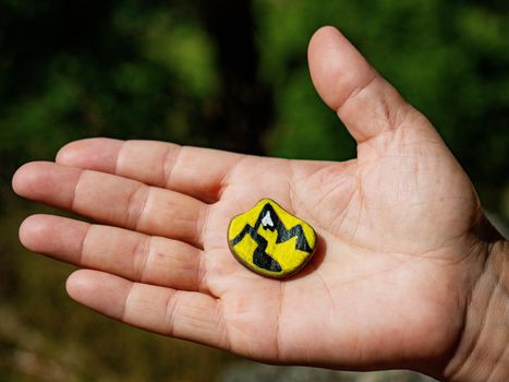 Hand palm holding chakra stone in heart shape with paint of mountains outline. Magic healing spiritual esoteric practice stone