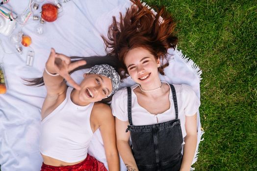 Two women having picnic together, laying on the plaid on the lawn