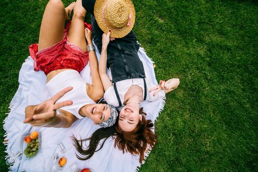 Two women having picnic together, laying on the plaid on the lawn