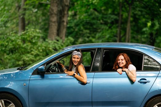 Two attractive young girlfriends fool around and laughing together in a car on a sunny day.