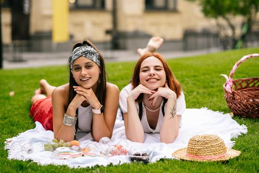 Two women having picnic together, laying on the plaid on the lawn