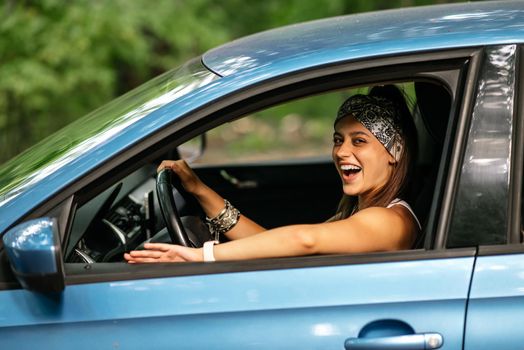 Portrait of of young woman looking at camera through window and sitting at the driver's seat