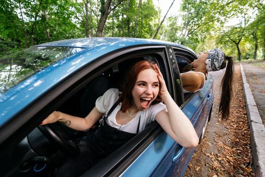 Two attractive young girlfriends fool around and laughing together in a car on a sunny day.