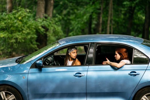 Two attractive young girlfriends fool around and laughing together in a car on a sunny day.