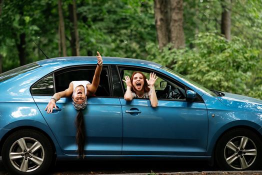 Two attractive young girlfriends fool around and laughing together in a car on a sunny day.