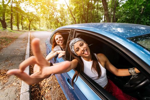 Two attractive young girlfriends fool around and laughing together in a car on a sunny day.