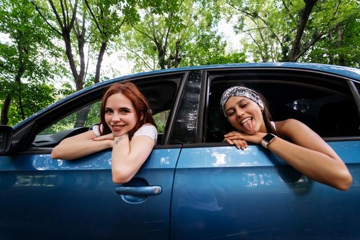 Two attractive young girlfriends fool around and laughing together in a car on a sunny day.