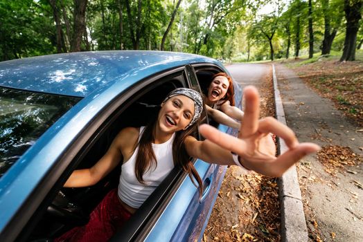 Two attractive young girlfriends fool around and laughing together in a car on a sunny day.