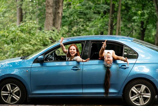 Two attractive young girlfriends fool around and laughing together in a car on a sunny day.