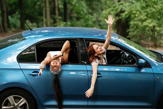 Two attractive young girlfriends fool around and laughing together in a car on a sunny day.