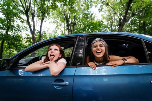 Two attractive young girlfriends fool around and laughing together in a car on a sunny day.