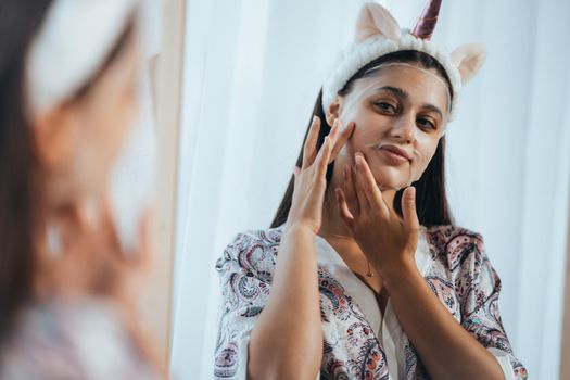 Young model applying cosmetic cream treatment on her face