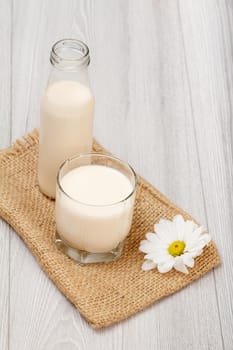 Bottle and glass of fresh milk, chamomile flower on sackcloth bag. Top view