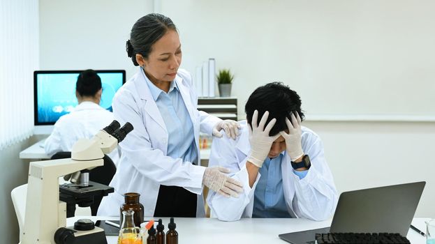 Senior woman scientist comforting stressed male having problems results of the experiment.