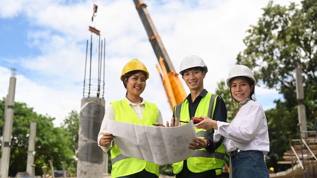 Civil engineer team in safety helmet standing at the construction site with crane and beautiful sky in background.