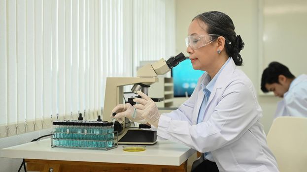 Professional specialist looking under microscope, conducting experiment in a laboratory.