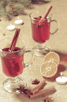 Glass of Christmas mulled wine with cinnamon, star anise and cloves on sackcloth with slices of orange, natural fir tree branches and cones. Color toning effect.