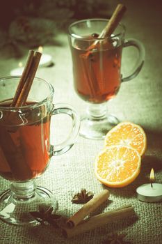 Glass of Christmas mulled wine with cinnamon, star anise and cloves on sackcloth with slices of orange, natural fir tree branches and cones. Color toning effect.