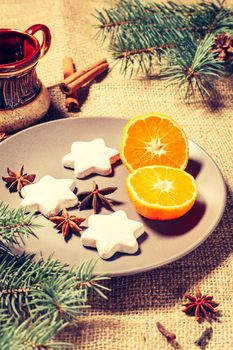 Gingerbread cookies in star shape on plate with cinnamon, star anise and natural fir tree branches with cones, cup of coffee on sackcloth. Color toning effect.