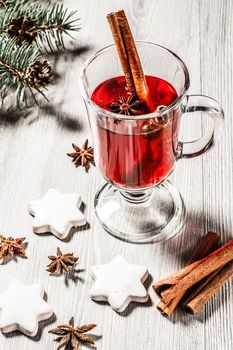 Glass of Christmas mulled wine with cinnamon, star anise and cloves on wooden background with white biscuits, natural fir tree branches and cones. Color toning effect.