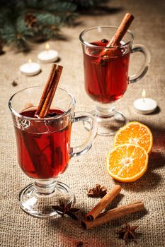 Glass of Christmas mulled wine with cinnamon, star anise and cloves on sackcloth with slices of orange, natural fir tree branches and cones. Color toning effect.