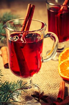 Glasses of Christmas mulled wine with cinnamon, star anise and cloves on sackcloth with slices of orange, white biscuits and natural fir tree branches on the background