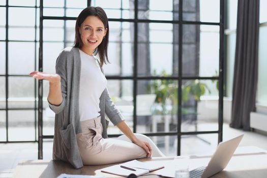 Image of young beautiful joyful woman smiling while working with laptop in office