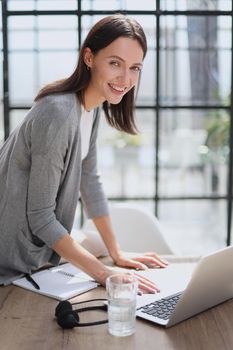 Image of young beautiful joyful woman smiling while working with laptop in office