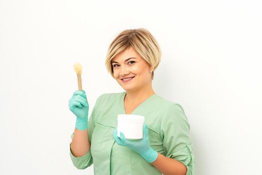 The master of sugar hair removal holds liquid yellow sugar paste, wax for depilation with the jar on a wooden stick on a white background